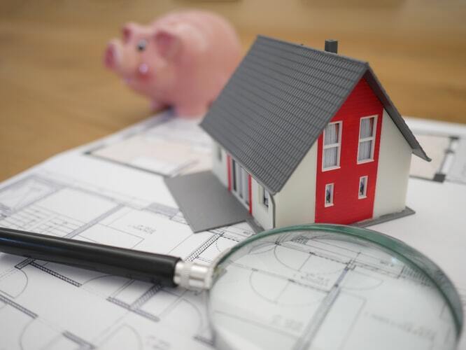house model on house plans with magnifying glass and piggy bank