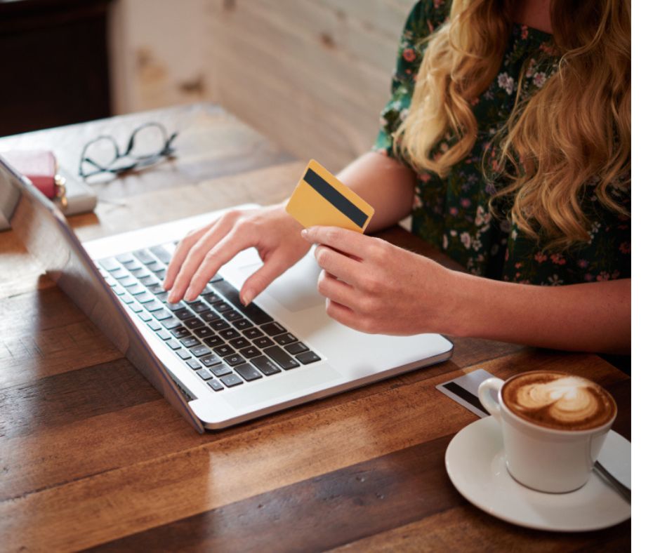 woman doing online grocery shopping sitting at laptop with coffee and credit card in her hand